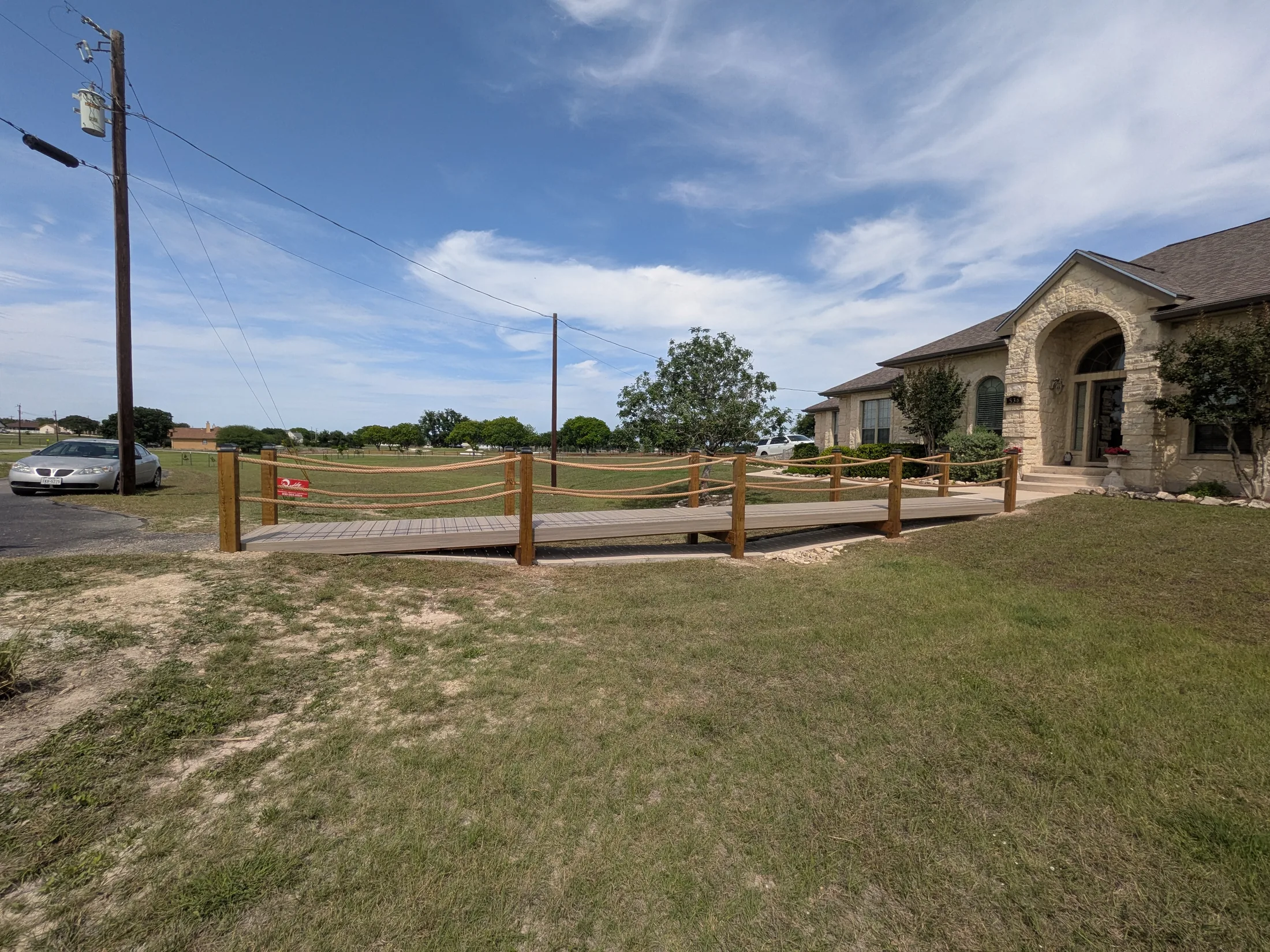 Finished raised boardwalk bridge with Trex decking and rope railing in front of Bandera home