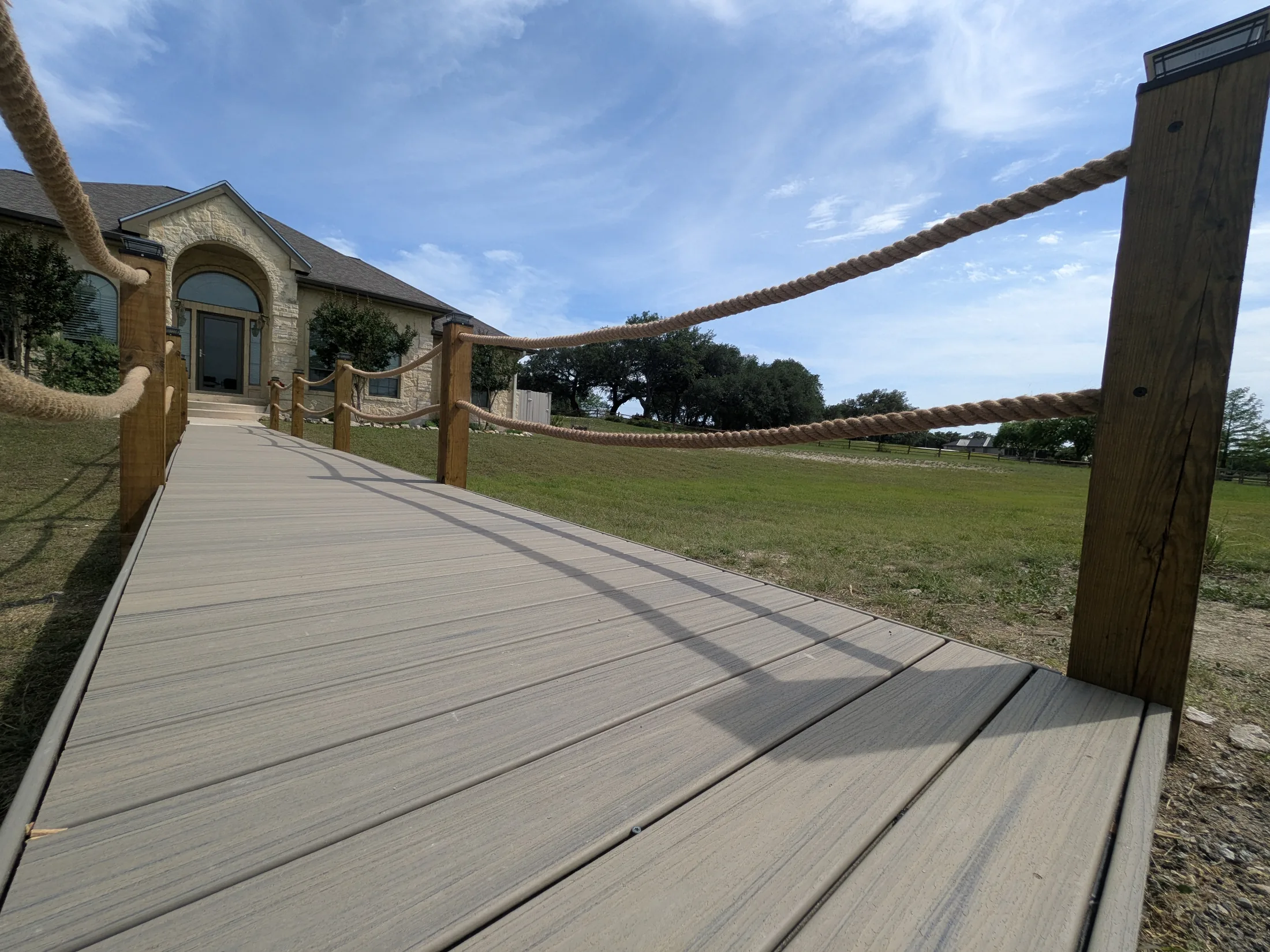 Finished raised boardwalk bridge with Trex decking and rope railings leading to a front entry in Bandera