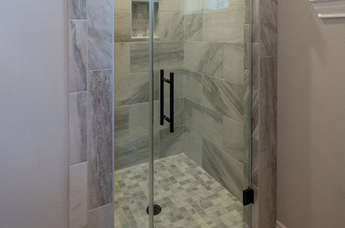 Small tile shower with white and grey tile and frameless glass door.